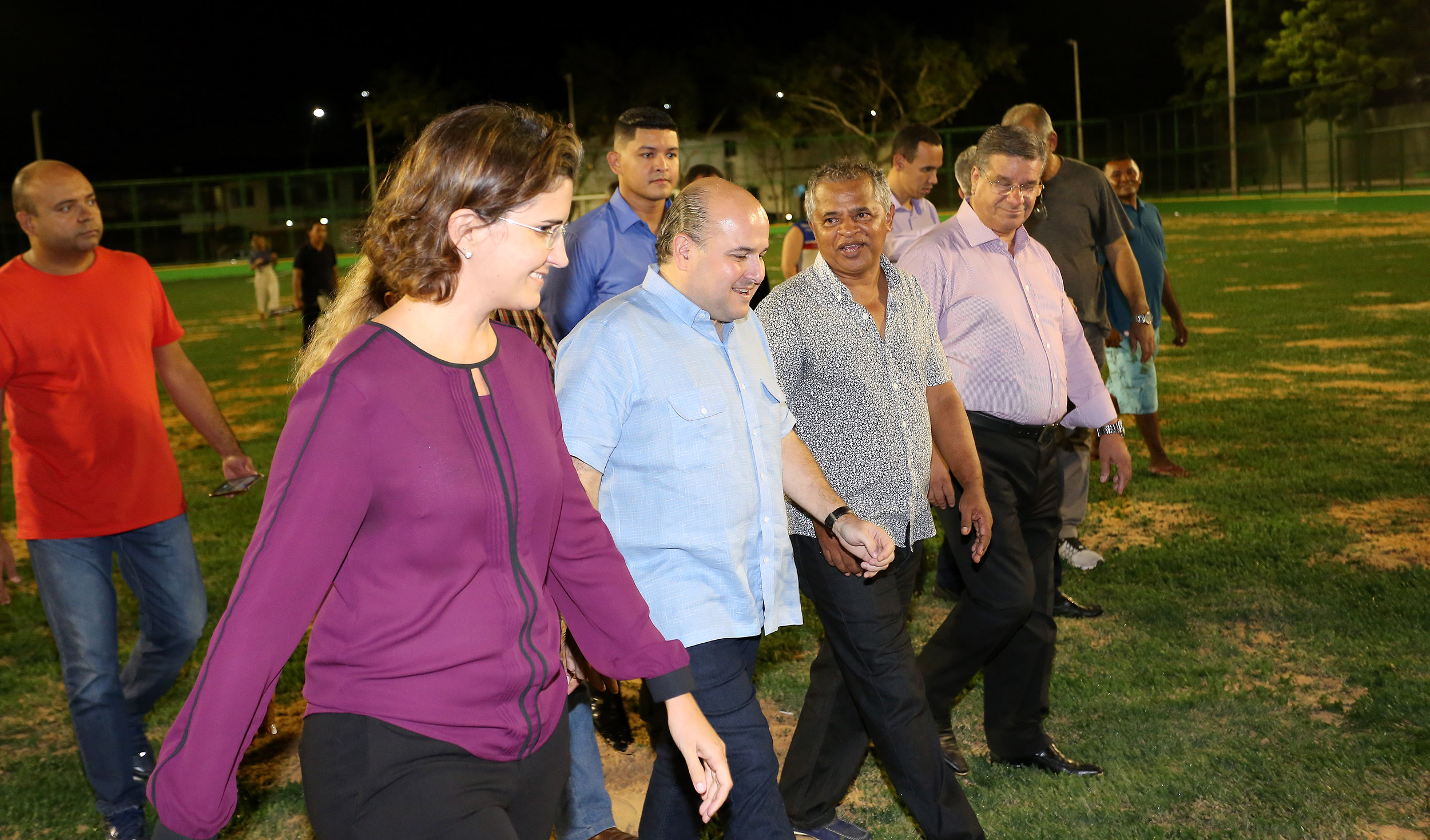 Um grupo de pessoas caminha pelo gramado do campo da areninha